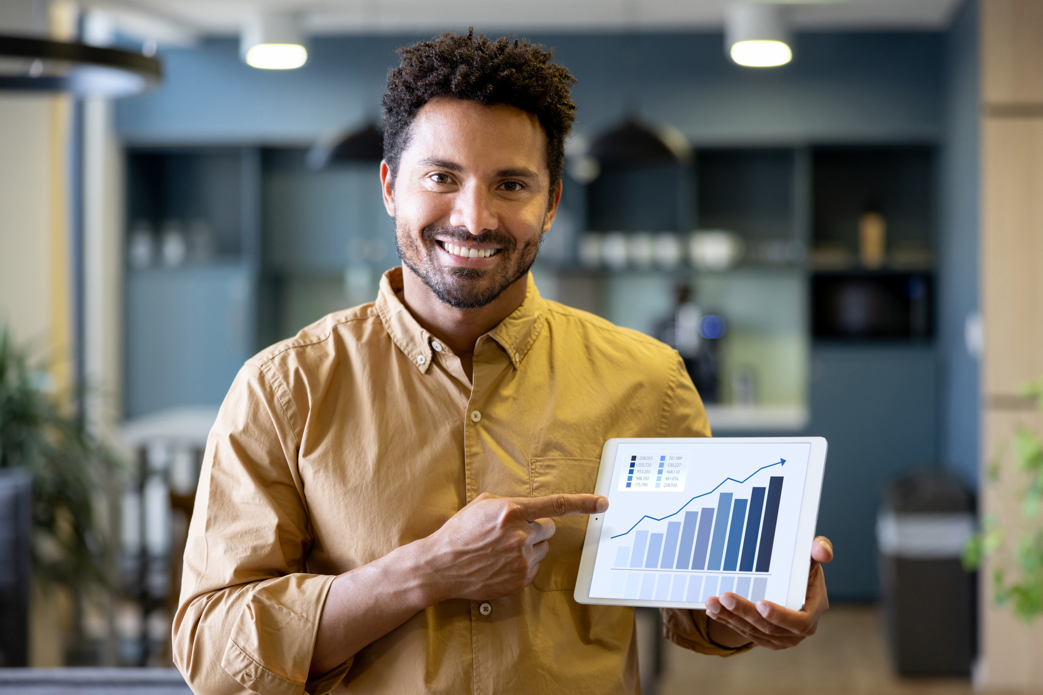 Portrait of a Latin American business man at the office pointing at a growth graph on a digital tablet