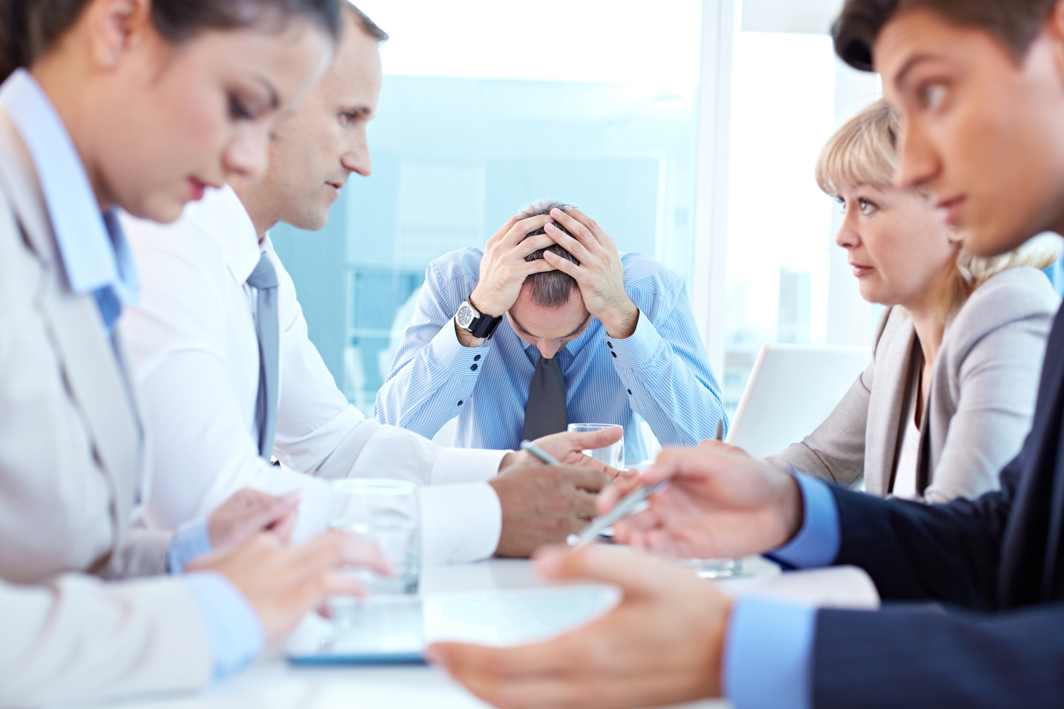 Stressed leader sitting at the head of table at staff meeting