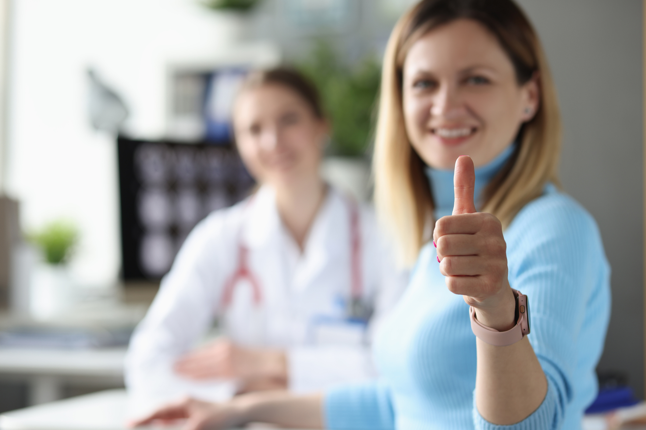 Woman patient demonstrates thumbs up gesture at doctor appointment. Diagnostic medical research concept