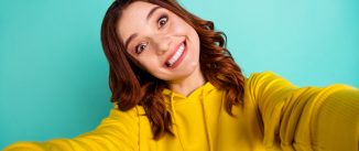 Photo of trendy cute cheerful nice millennial smiling toothily showing teeth with face expression, of joyfulness while taking selfie isolated over teal vivid color background