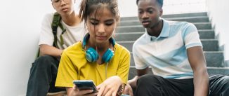 Three teenager African and Asian High School friends watching smartphone together in the School Staircase