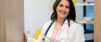 Beautiful middle aged female doctor holding a document and opening the door looking at camera smiling very happy