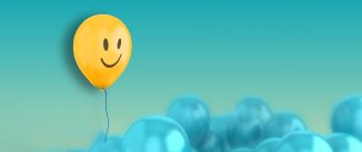 A large group of blue baloons with a yellow one with a smiley face on it floating above the rest
