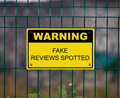 Yellow warning sign on a fence stating : Warning, Fake reviews spotted.