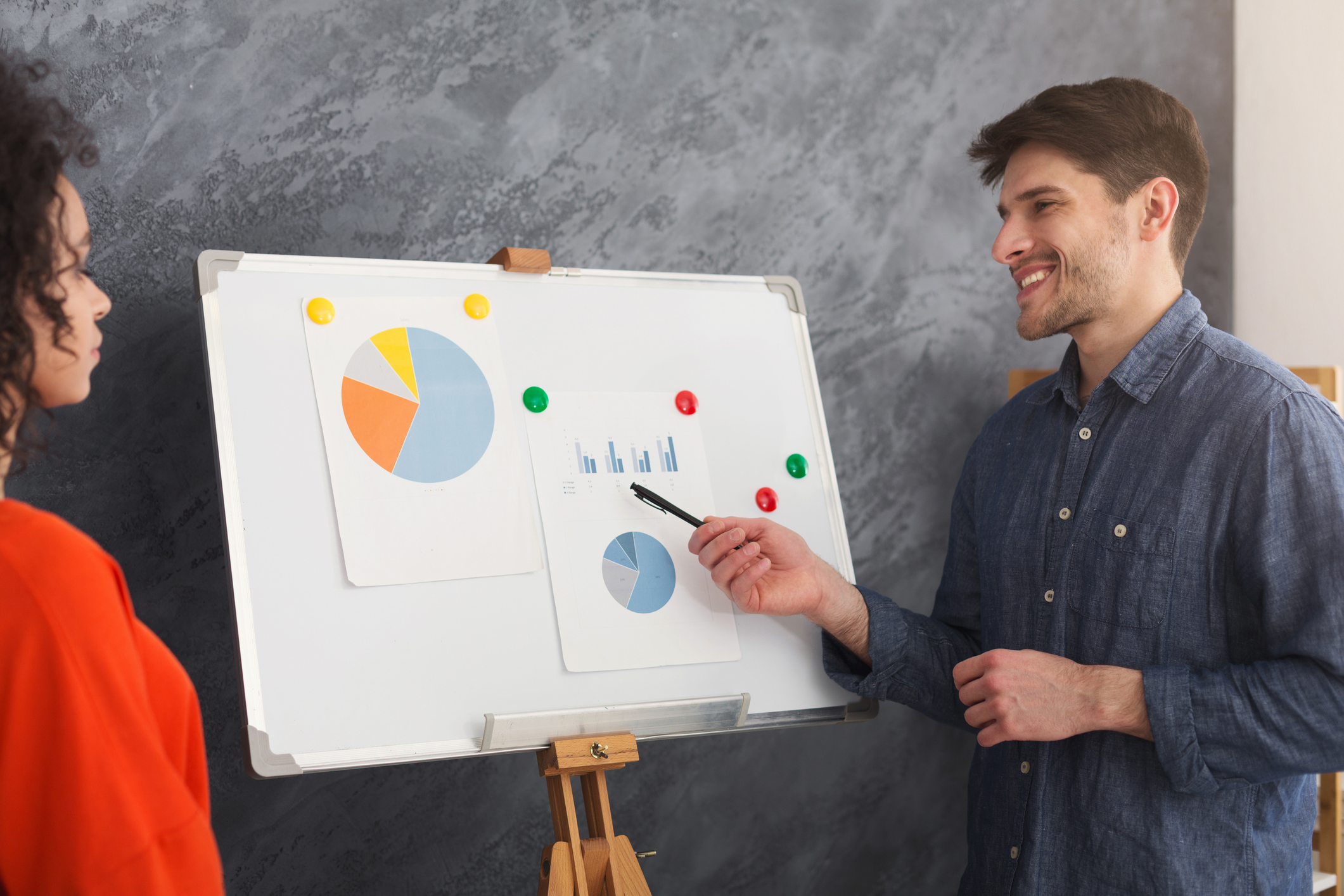 Young cheerful businessman giving presentation to colleague in board room. Two multiethnic partners discussing sales chart in office, copy space