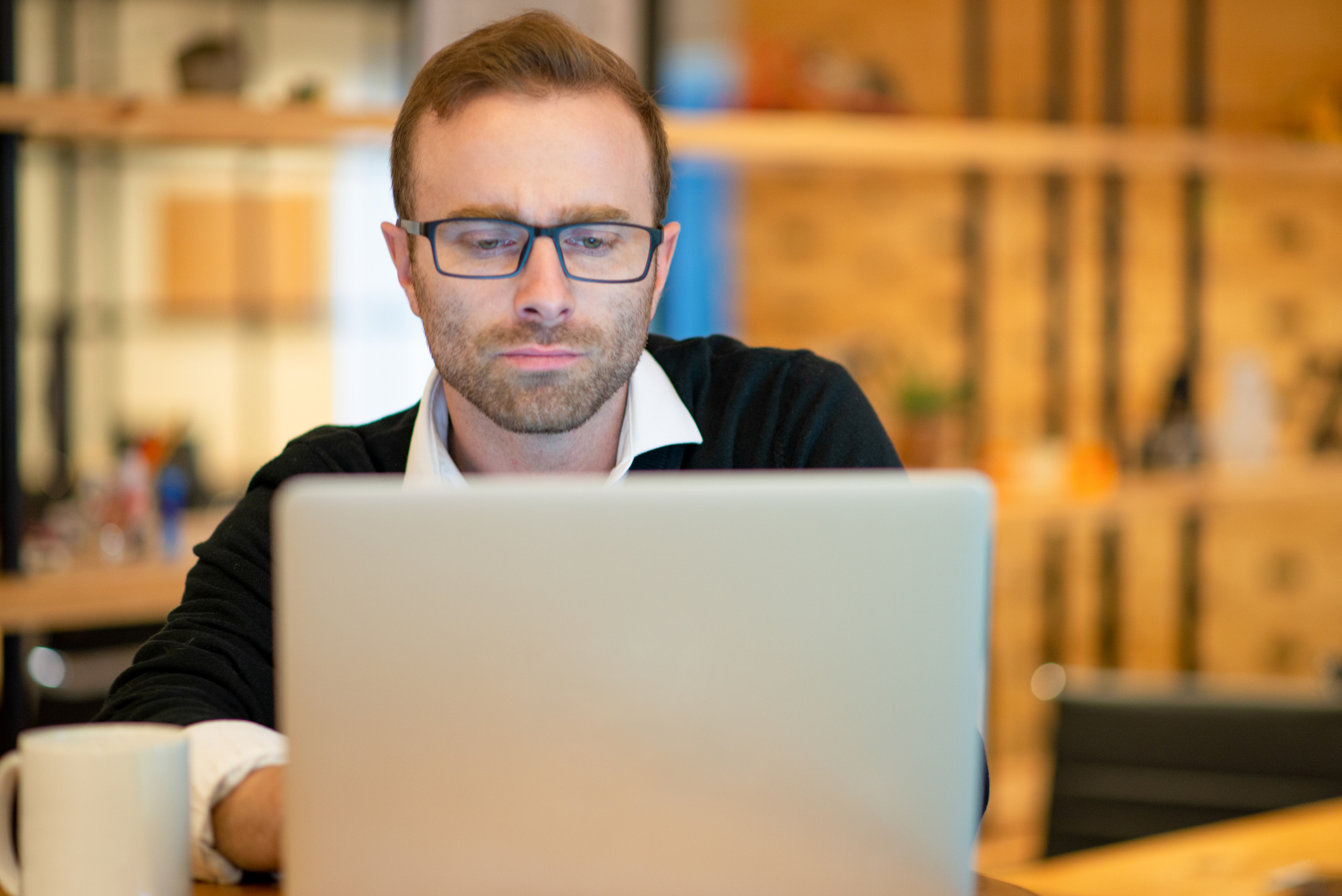 Focused middle-aged businessman working on laptop computer. Businessman sitting at table with blurred interior in background. Freelance concept. Front view.