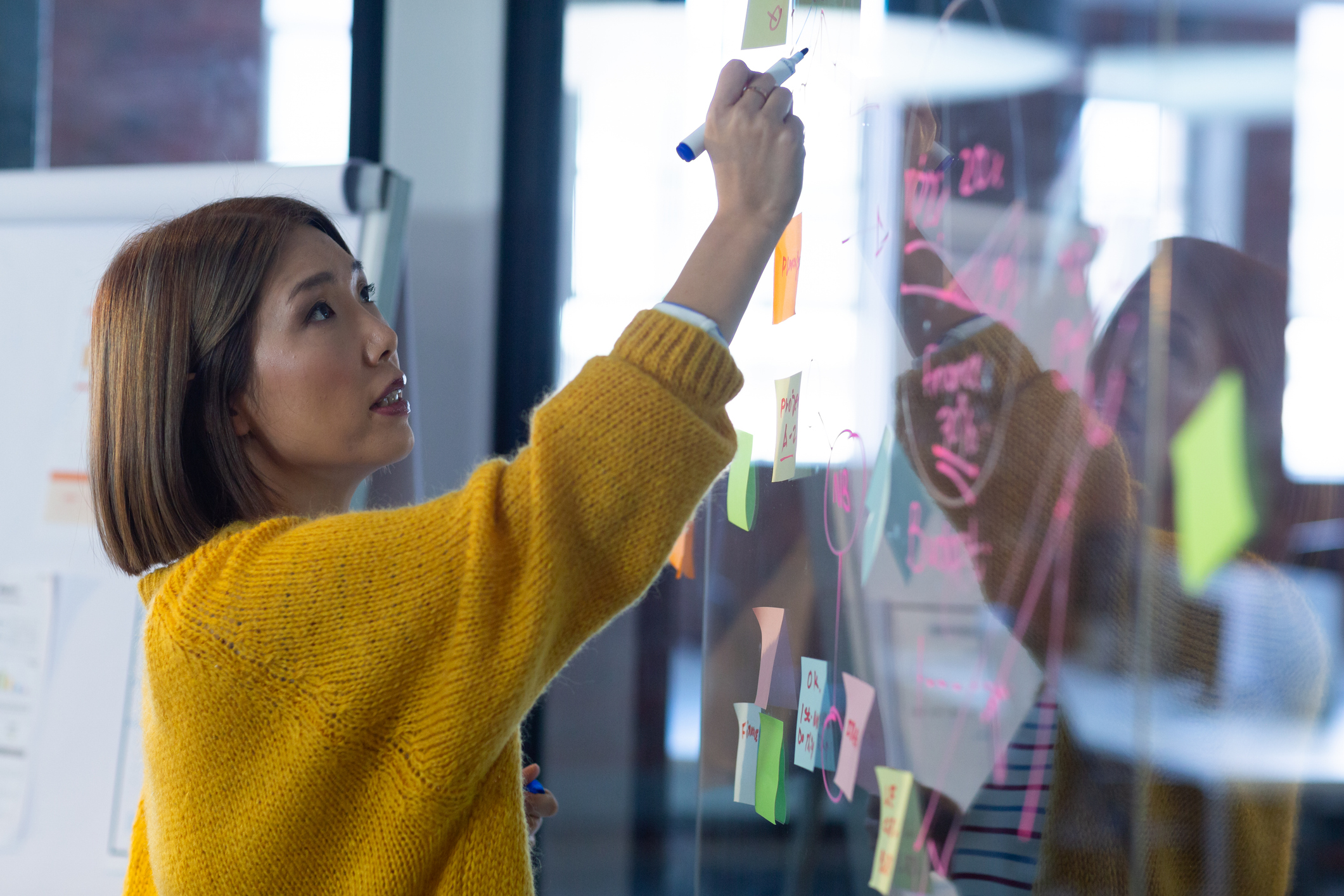 Asian businesswoman standing in front of glass wall and writing in office. independent creative design business.