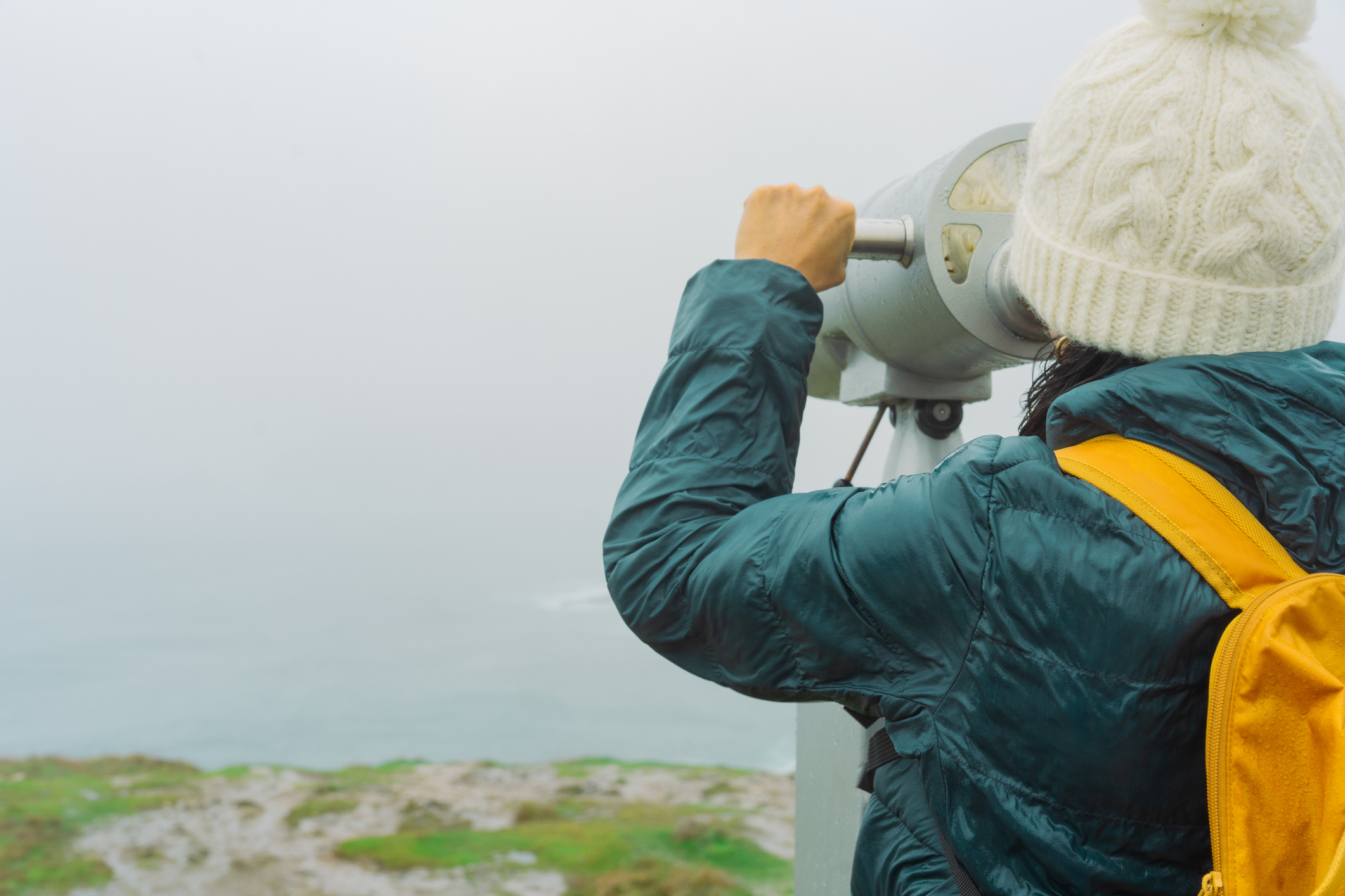 Unknown woman looking through a tourist binocular from high up on the Irish coast on a foggy day