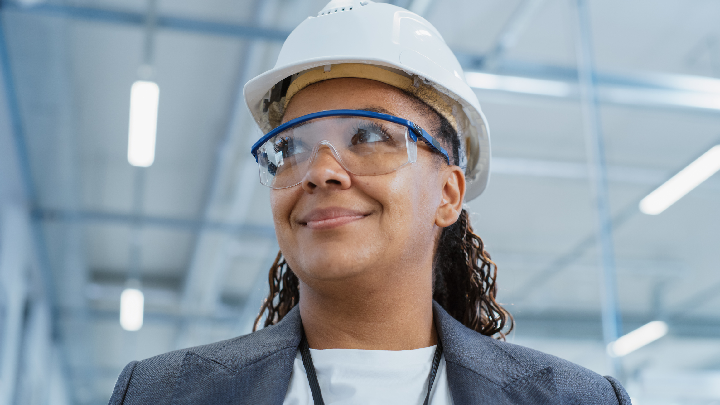 Close Up Portrait of a Middle Aged, Happy Black Female Engineer Putting On a White Hard Hat, While Standing at Electronics Manufacturing Factory. Heavy Industry Specialist Posing for Camera.