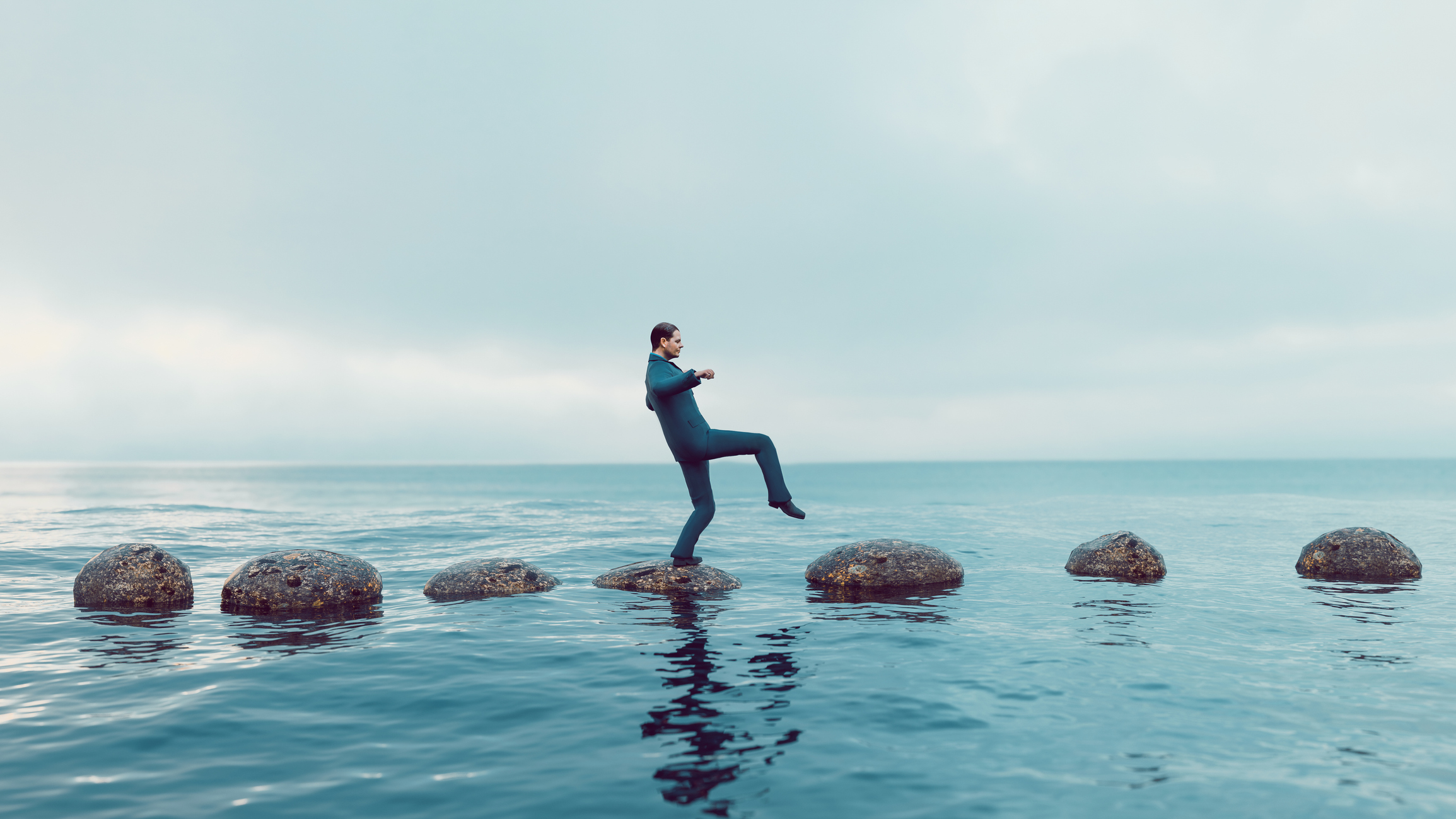 Man walks carefully on a path of small rocks in the middle of the sea. He looks focused and moves in the right direction. Concept of success and avoiding problems on the way of a journey or career path.