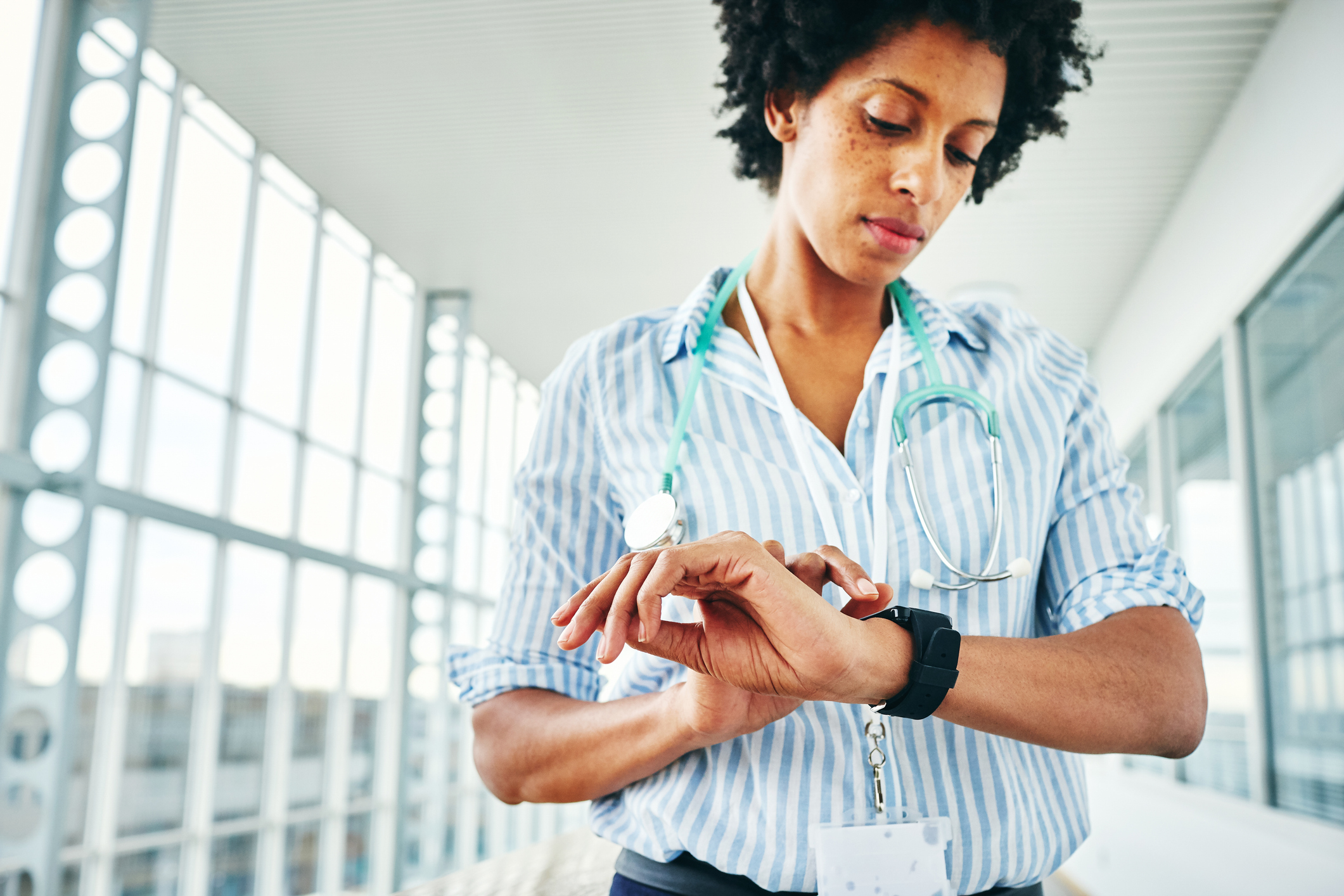 African female physician checking her digital wrist watch while standing in hospital corridor