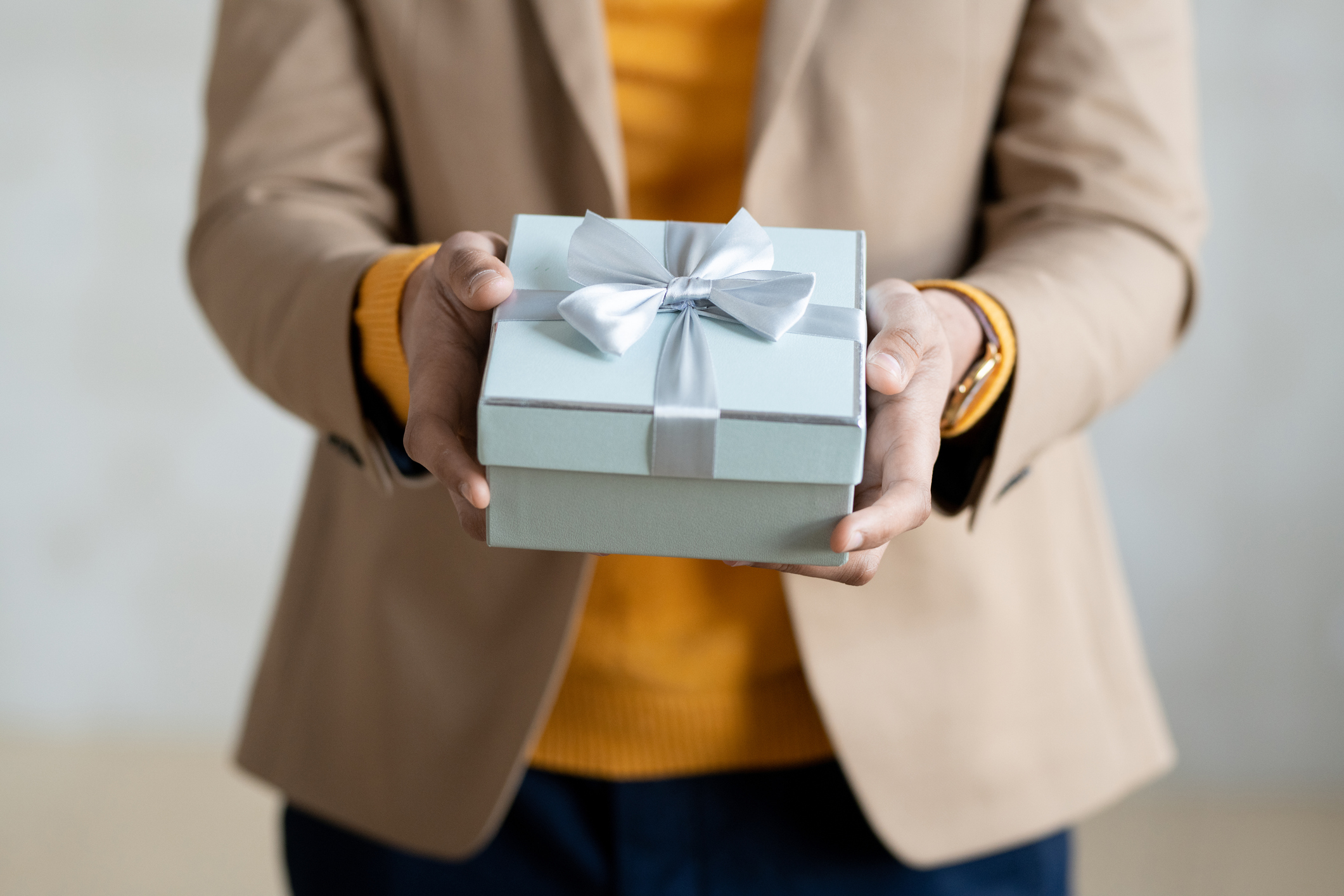 Hands of young elegant businessman with packed birthday present in giftbox passing you gift in blue box with bow made up of silk ribbon