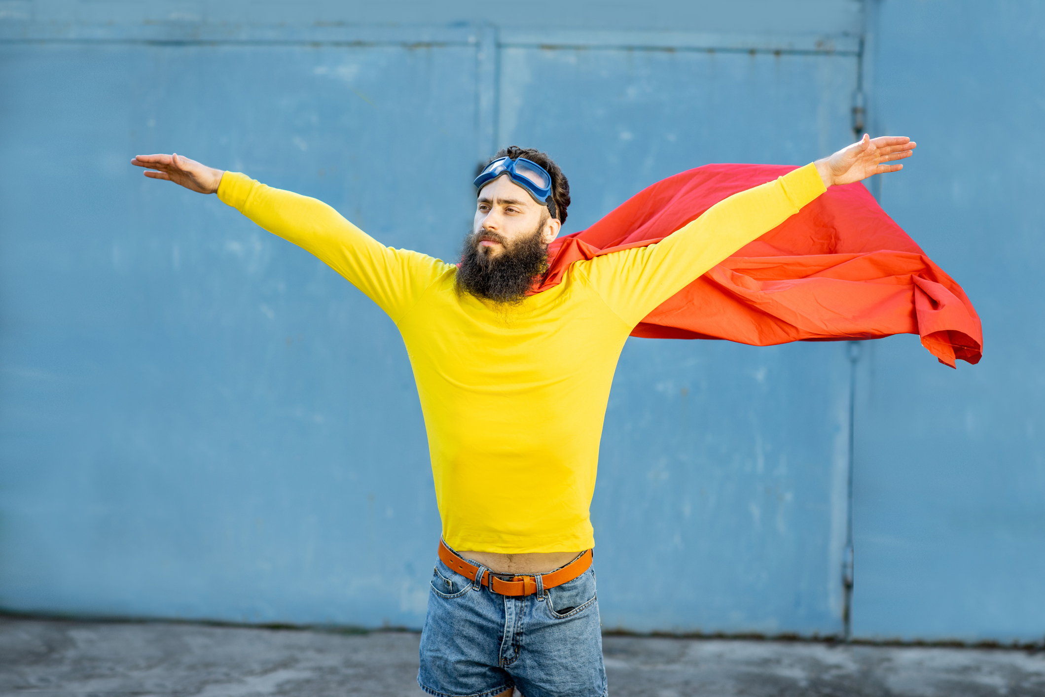 Portrait of a man like a superhero in colorful clothes and pilot's glasses on the blue background