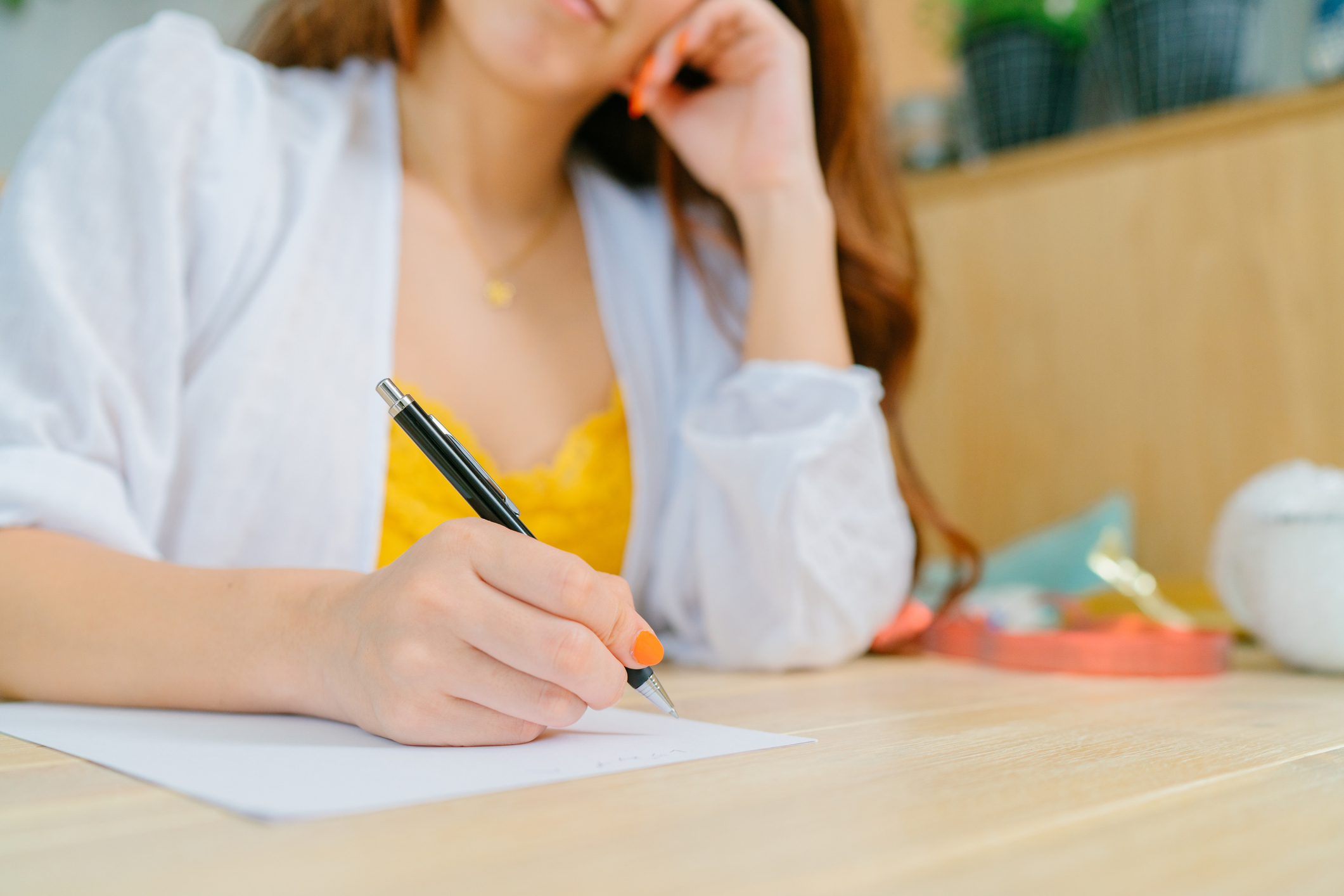 A close-up photo of a young woman`s hand while writing a letter to put inside a gift box in the living room at home