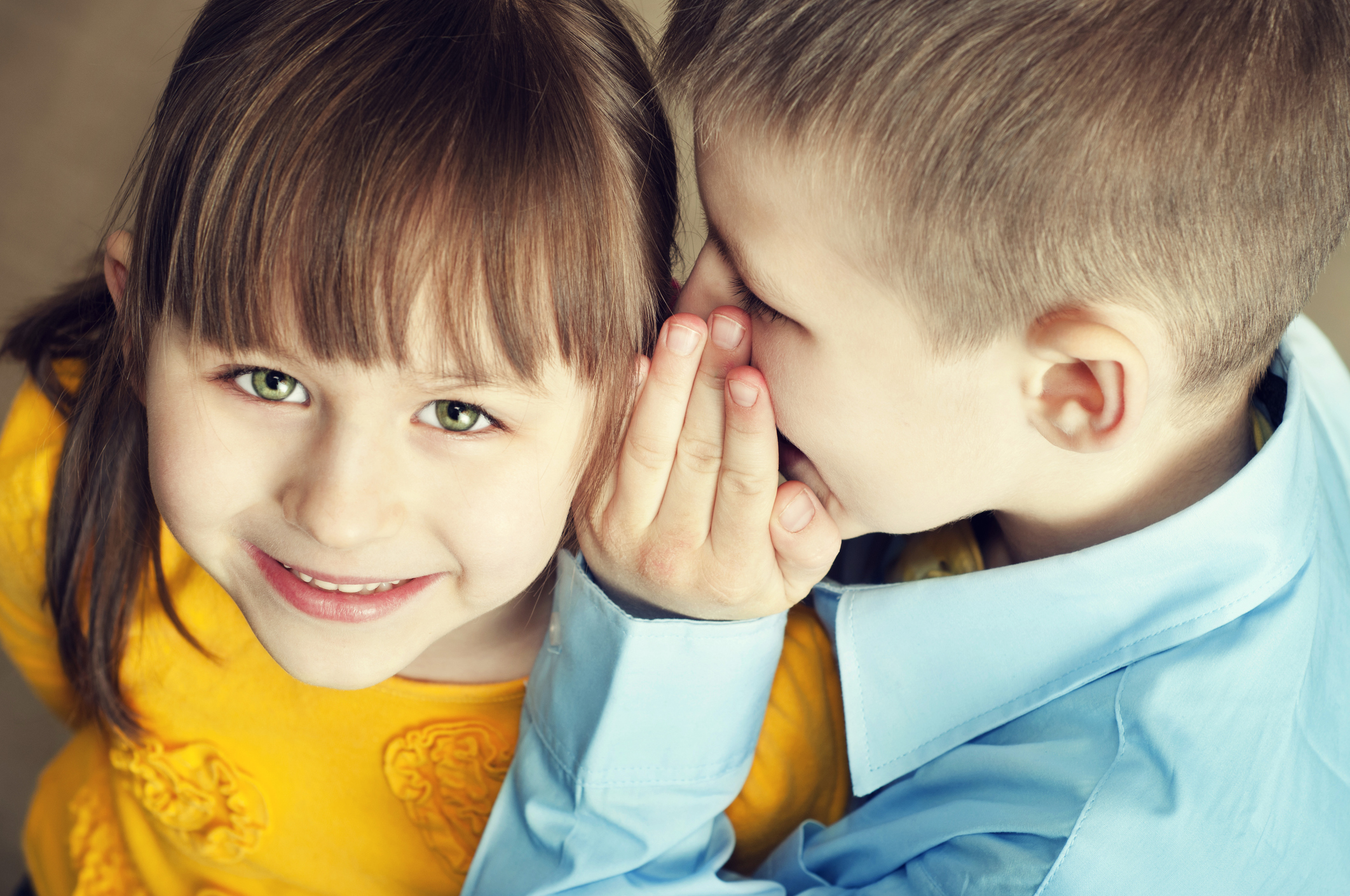 Little boy whispering to his sister's ear.