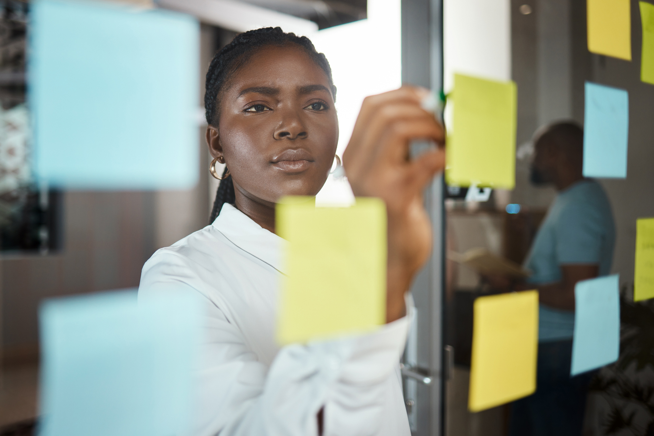 A businesswoman writing on a yellow postit note on a glass screen