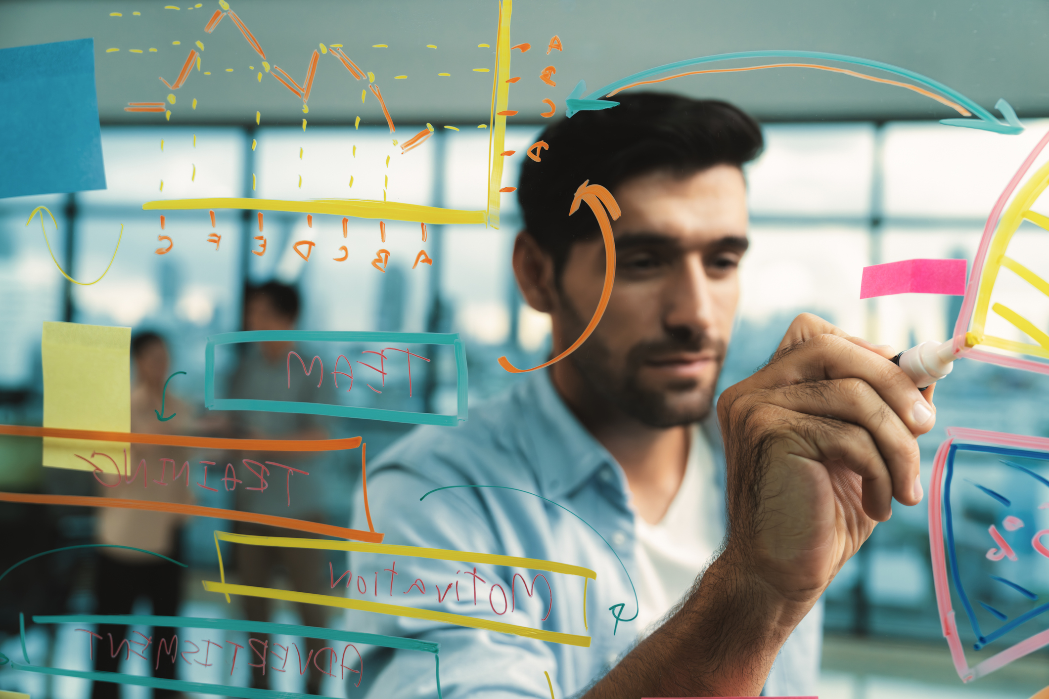 Portrait of young handsome businessman writing marketing idea by using colorful marker on glass wall with graph and mind map. Manager sharing idea or financial strategy. Business plan. Tracery.