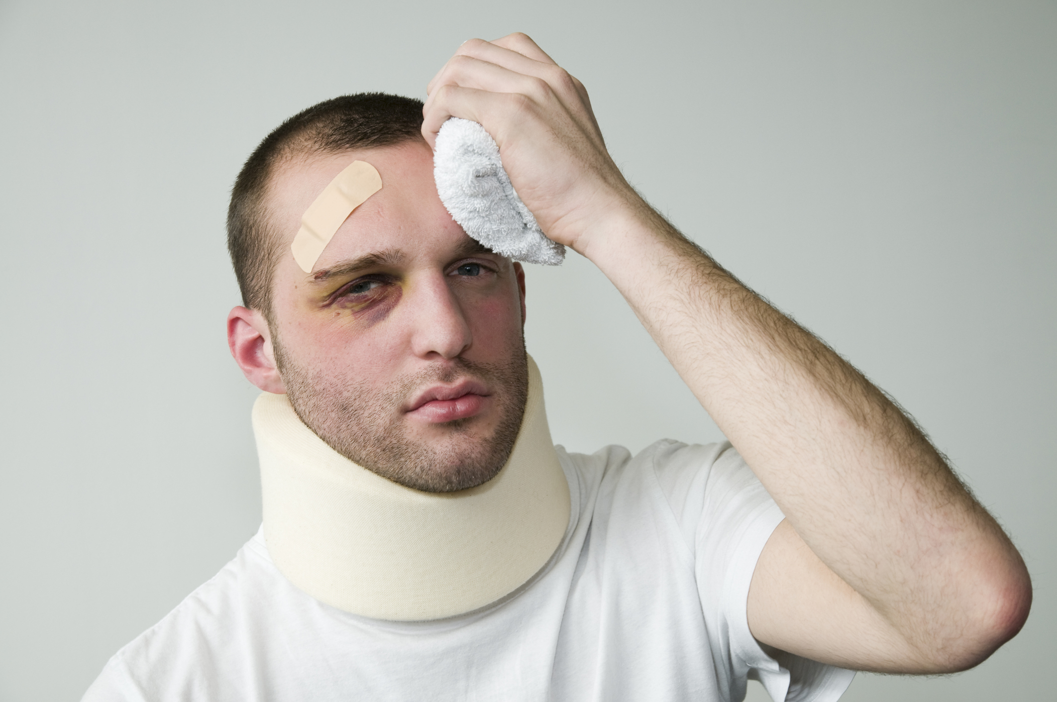 A beat-up young man in white wearing a neck brace and holding an icepack to his head