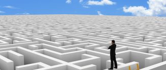 A businessman standing atop a large, white maze extending to the horizon against a blue sky.