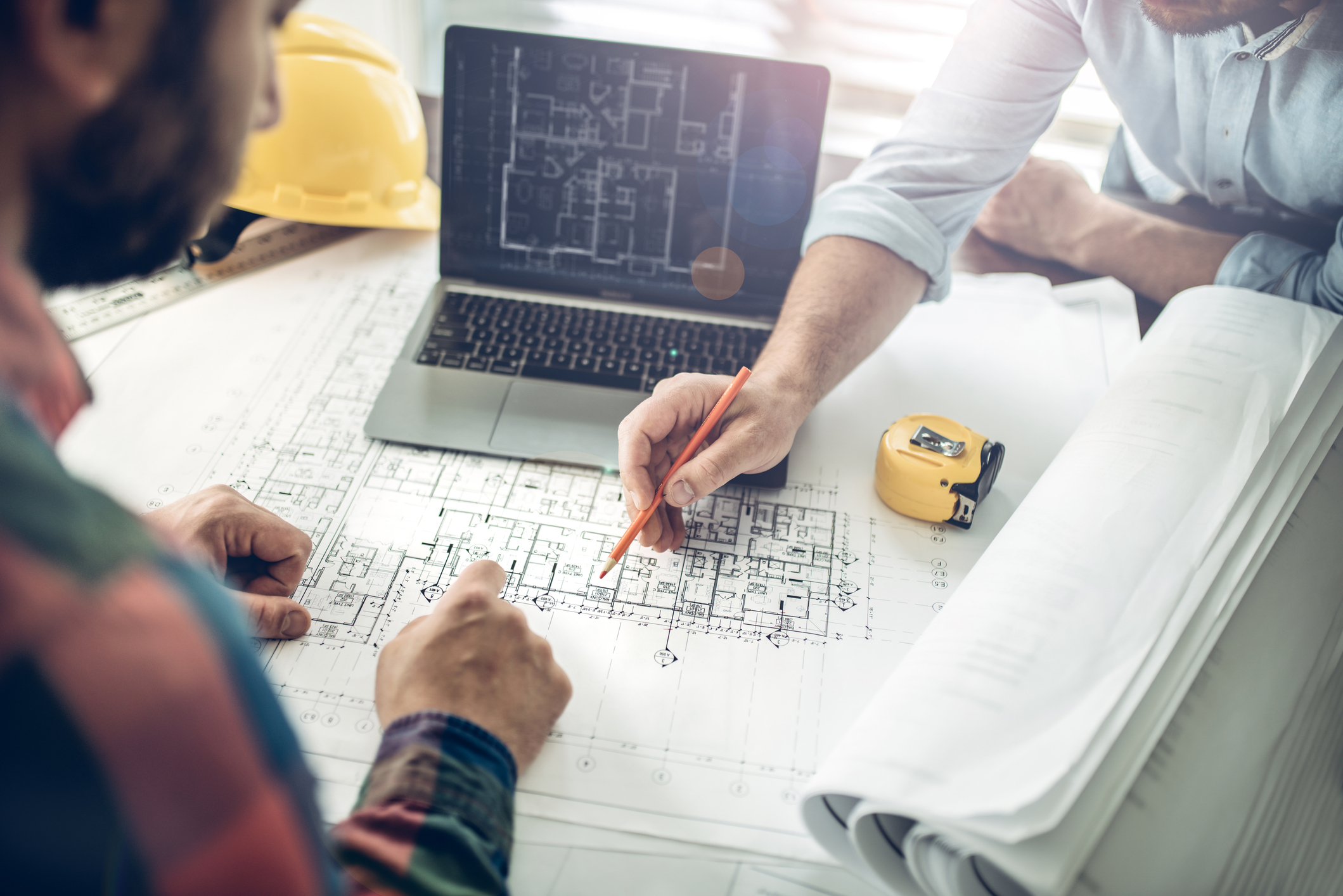 Hands of an architect and a building contractor pointing at the architectural plan on the screen. They have a coordination meeting to solve the site problems