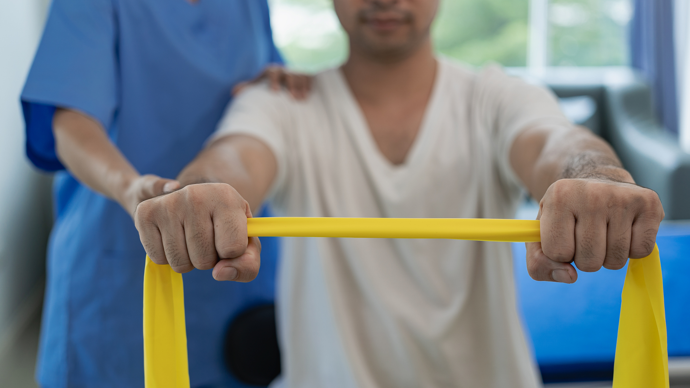 Handsome man exercising with dumbbells and stretching straps smiling in hospital department. Attractive nurse is helping him, orthopedic doctor helps do physical therapy, physical therapy in the clinic. Scoliosis treatment