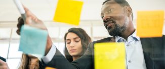 Close-up of smiling African businessman brainstorm meeting with colleagues by using colorful sticky paper note on glass wall for finding new ideas. Using agile methodology and do business.